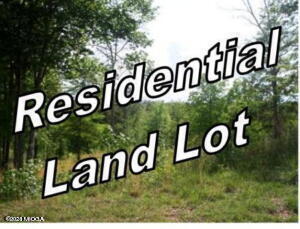Diagonal sign reading 'Residential Land Lot' across a wooded, grassy lot.
