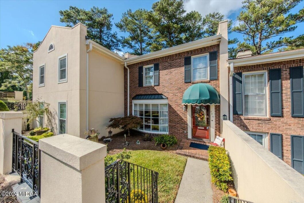 Brick townhouse with green canopy over the front door, bay window, and landscaped front yard under a blue sky.