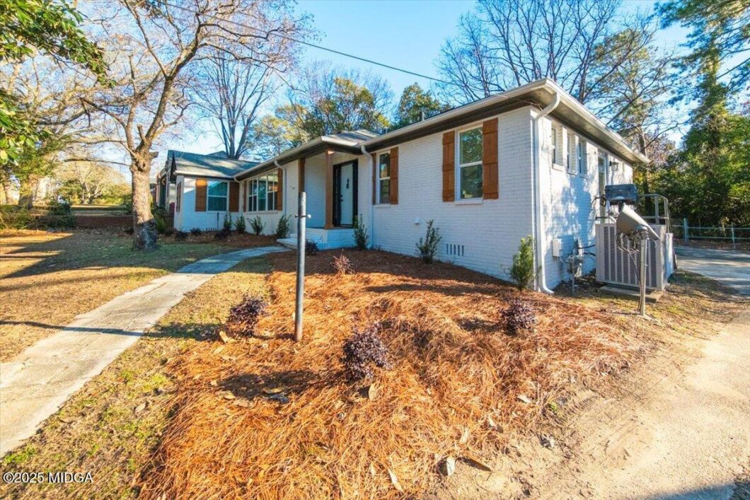 White brick single-family home with brown window shutters, a blue front door, and a concrete walkway to the entrance.
