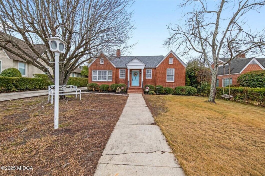 Front view of a brick ranch house with a light blue front door, a straight concrete walkway, and leafless trees in a manicured yard.