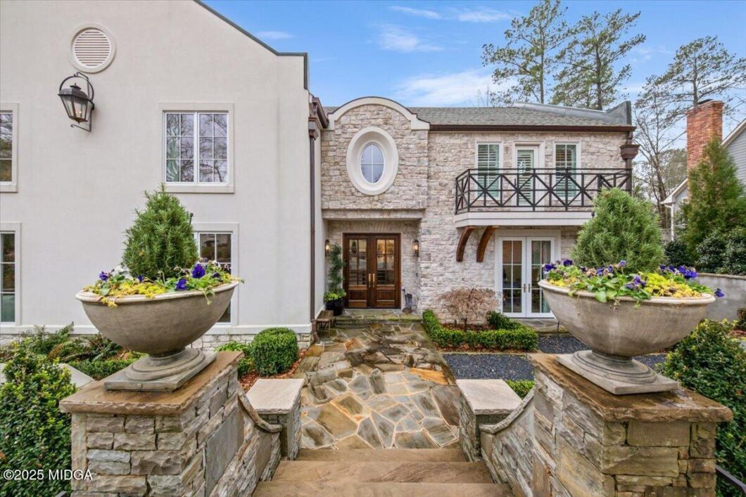 Stone-and-white townhouse entrance with large stone urn planters, stairs, and a wooden double door.