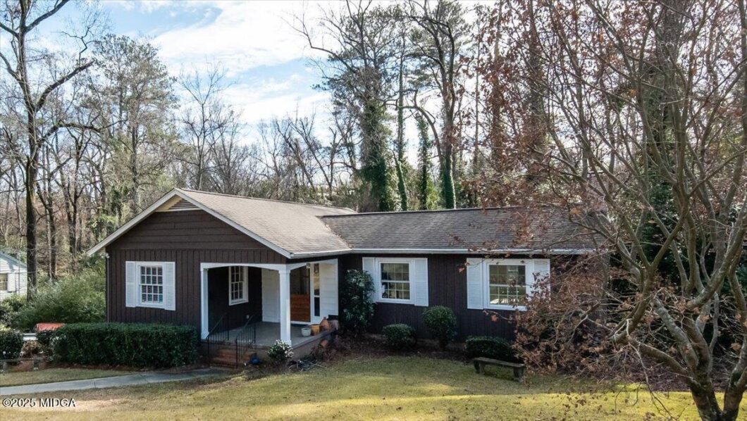 Single-story brown house with white shutters and a covered front porch, set in a yard with leafless trees.