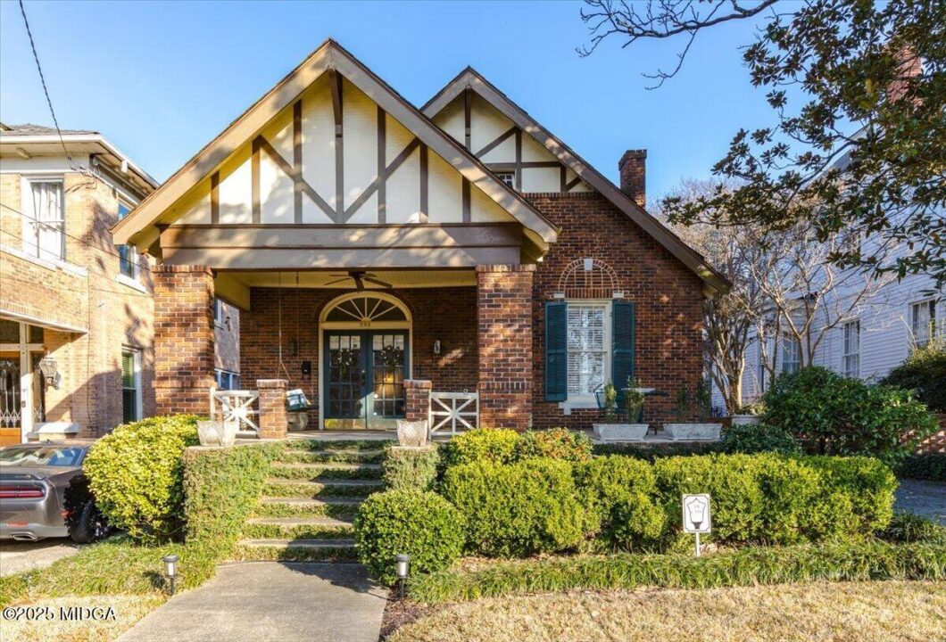 Brick craftsman-style house with a covered front porch, brick steps, and neatly trimmed hedges leading to the entrance.