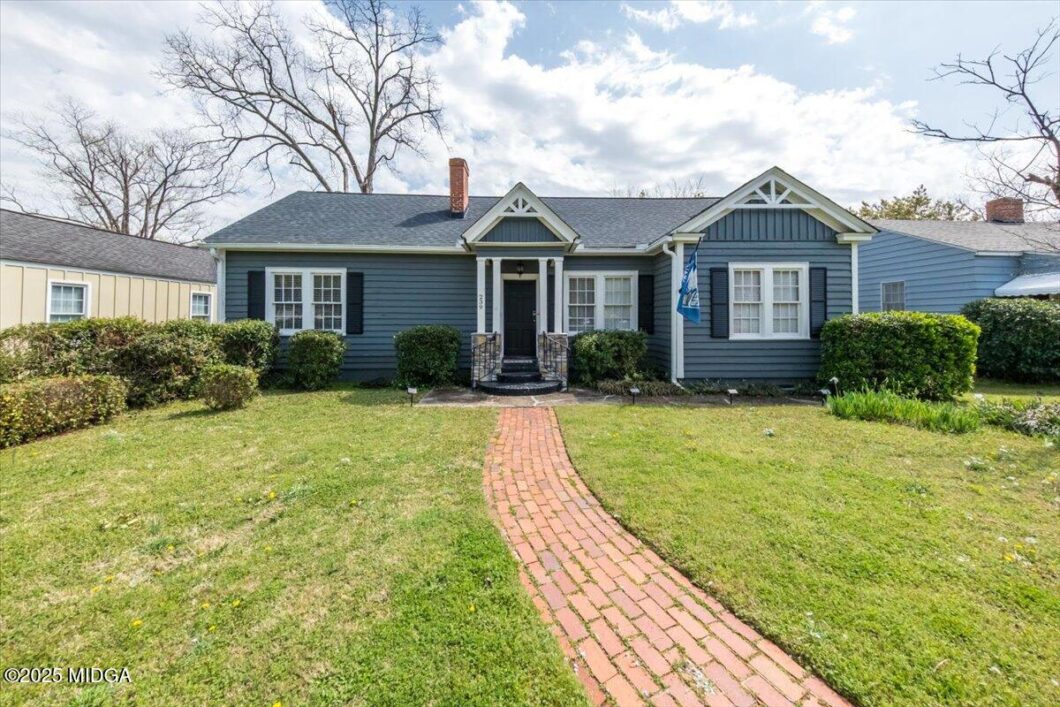 Blue single-story house with dark front door, brick curved walkway, and trimmed shrubs in a suburban yard.