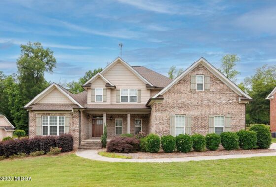 Front view of a two-story brick-and-siding suburban house with a manicured lawn and shrubs in front of the yard—blue sky above.