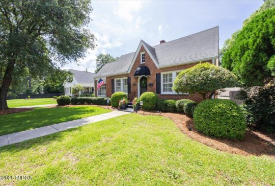 Brick cottage-style house with manicured shrubs, American flag, and a stone path leading to the front door. (Front view of a suburban home)