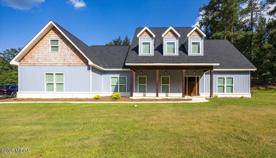 Front view of a blue house with a dark pitched roof, three dormer windows, and a covered porch on a green lawn.