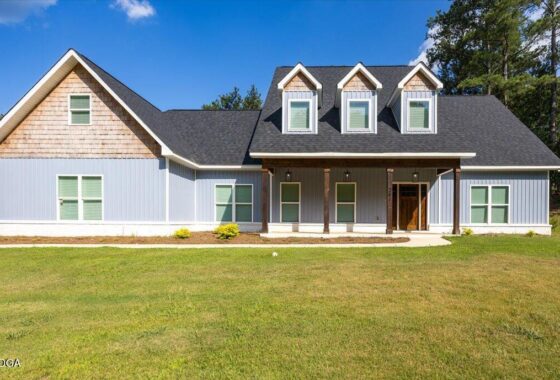 Front view of a blue house with a dark pitched roof, three dormer windows, and a covered porch on a green lawn.