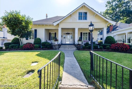 White cottage-style house with a front porch, columns, and manicured landscaping; walkway leads to the entrance.