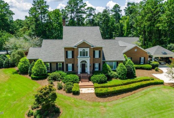 Large brick two-story house with a centered front door, flanked by trimmed shrubs and a manicured lawn.