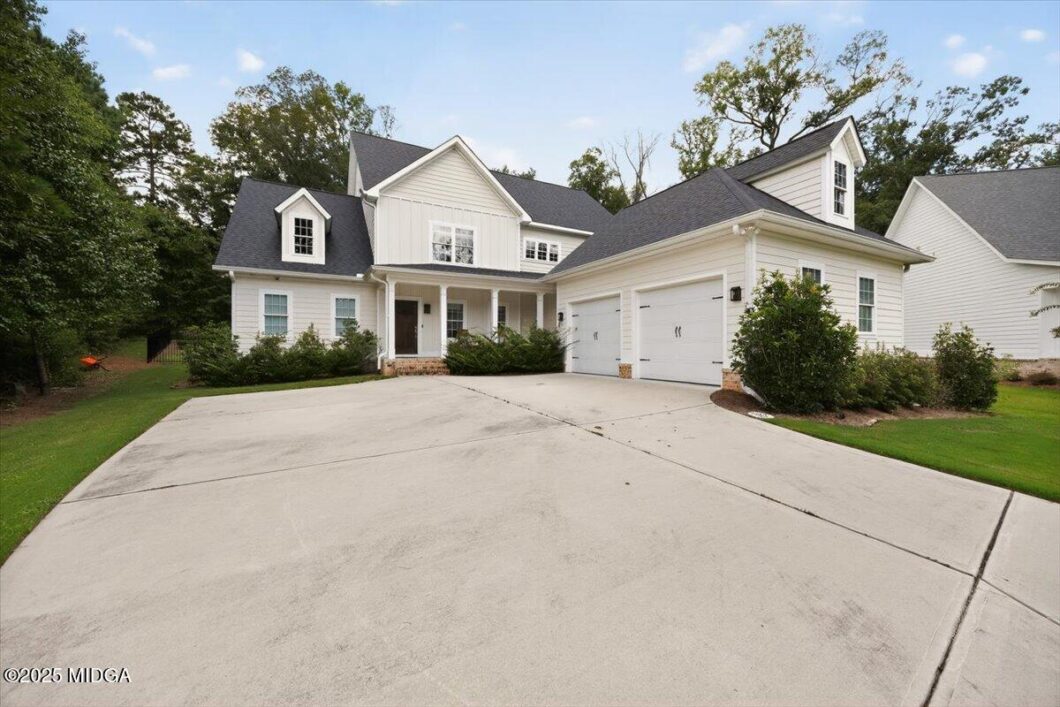 White two-story house with a three-car garage, front porch, and a green lawn.