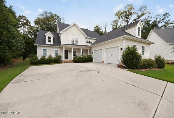 White two-story house with a three-car garage, front porch, and a green lawn.