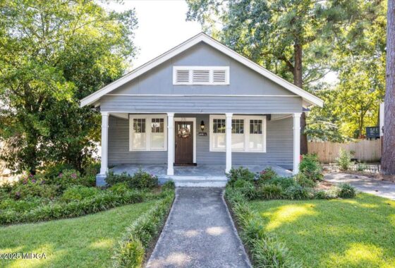Gray Craftsman-style house with white trim and a front porch, wreath on the door, and a walkway through a green lawn.