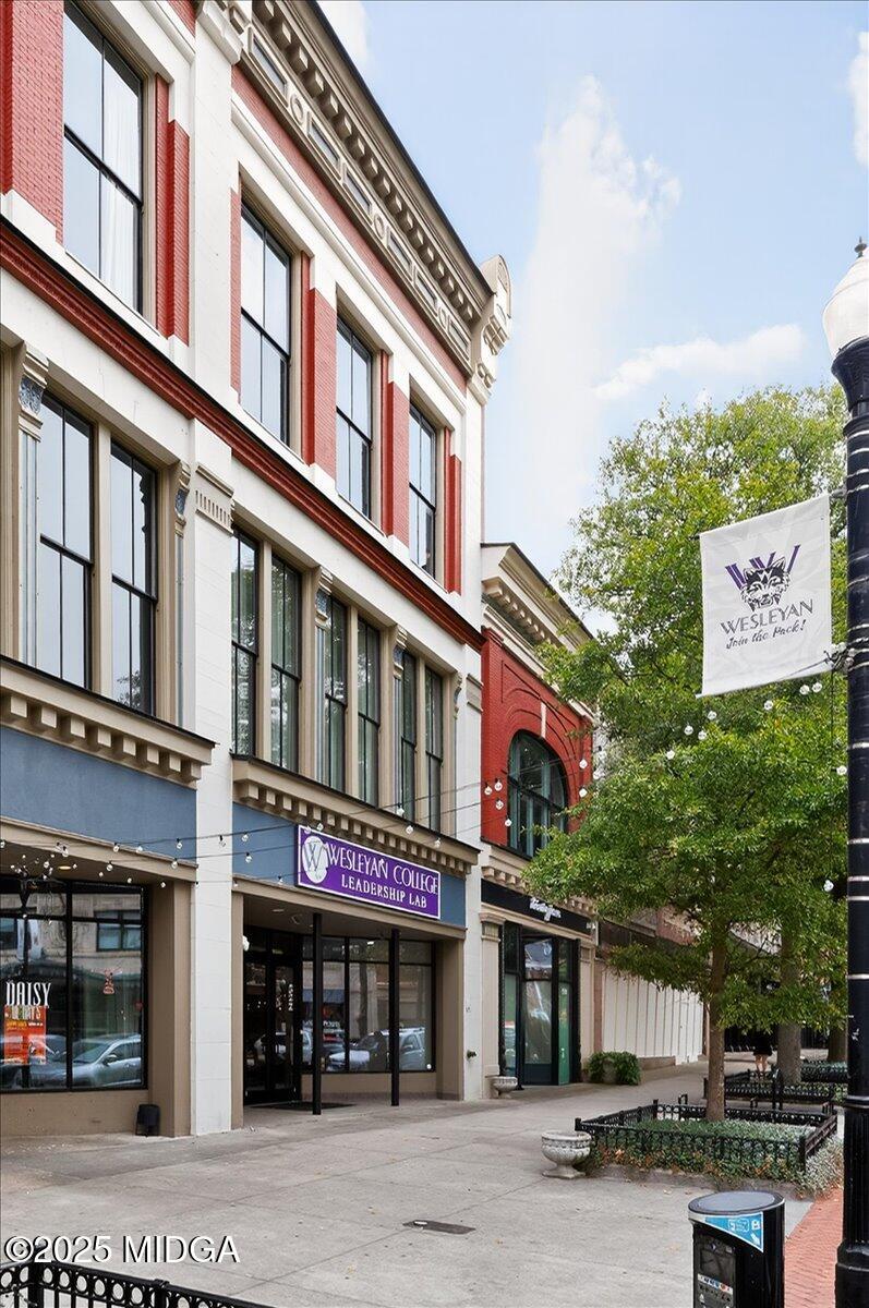 Urban street scene with brick storefronts; a Wesleyan College Leadership Lab sign is above the entrance. A white flag with the Wesleyan logo hangs by a tree on the right.