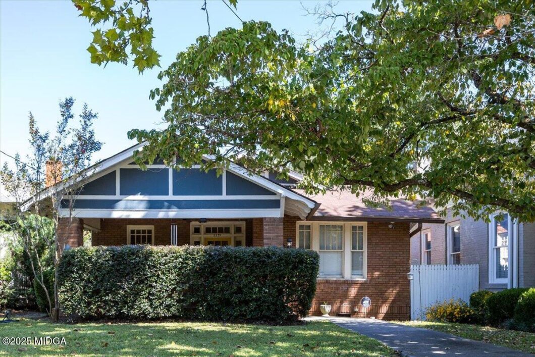 Brick bungalow with a covered front porch, blue gable trim, and a tall hedge in front. If there’s a label: avoid extra details.