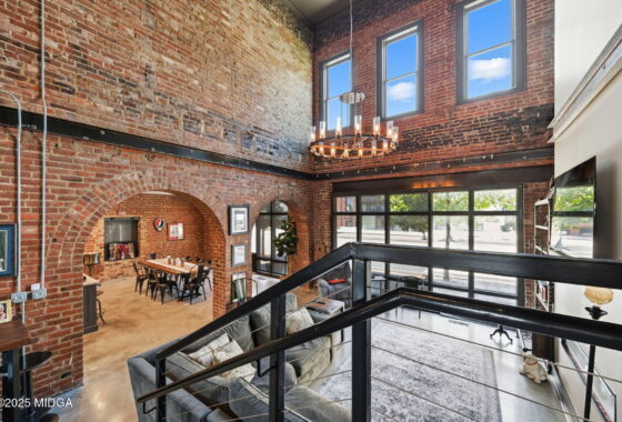 Industrial loft interior with exposed brick walls, arched brick doorways, and a circular chandelier seen from a mezzanine level.