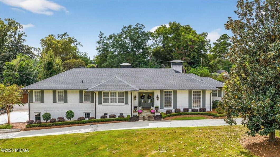 Single-story white brick house with a gray shingled roof, a small front porch, and landscaped front yard.