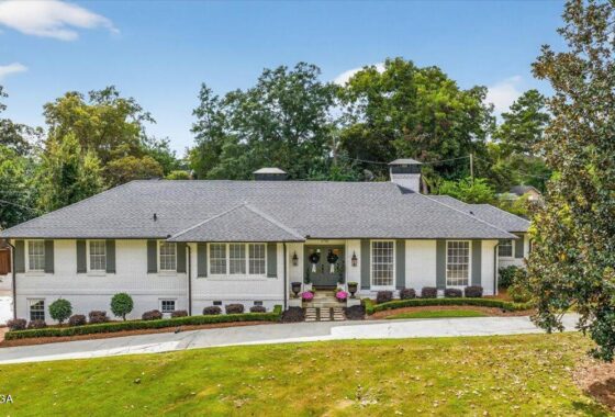 Single-story white brick house with a gray shingled roof, a small front porch, and landscaped front yard.