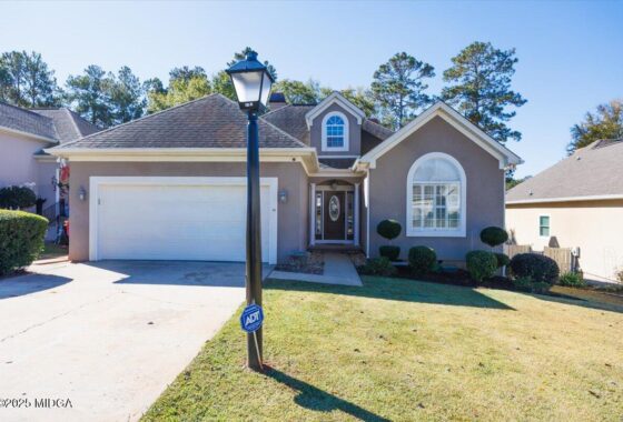 Suburban house with gray exterior, attached two-car garage, and well-kept front yard under a clear blue sky.
