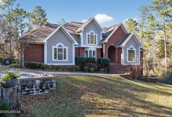 Front view of a two-story brick-and-gray house with arched windows and a curved brick entryway, set on a wooded lot.