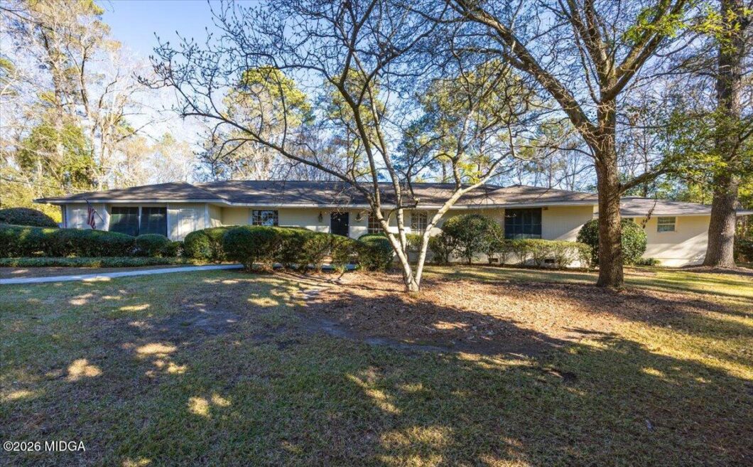 Single-story beige house with a flat roof, front yard, and leafless trees casting shadows on a sunny day.