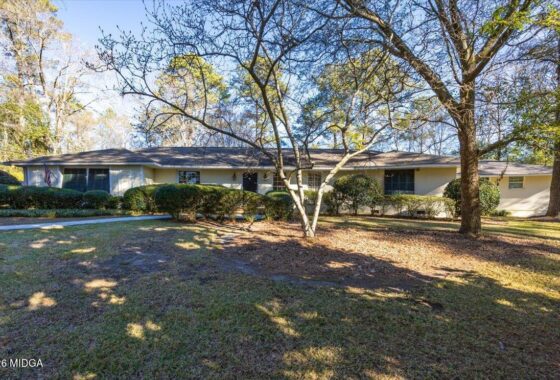 Single-story beige house with a flat roof, front yard, and leafless trees casting shadows on a sunny day.