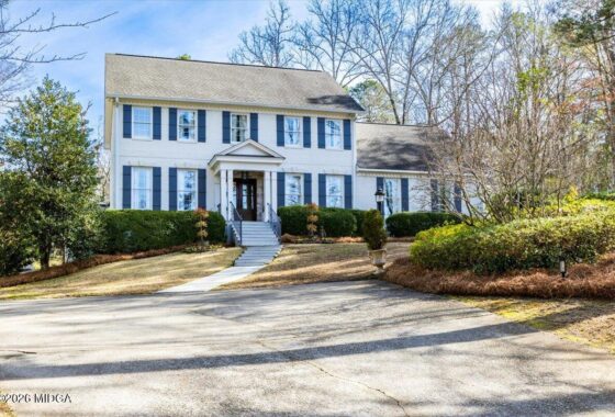 White two-story house with blue shutters, centered front door, and manicured hedges along the entry steps.