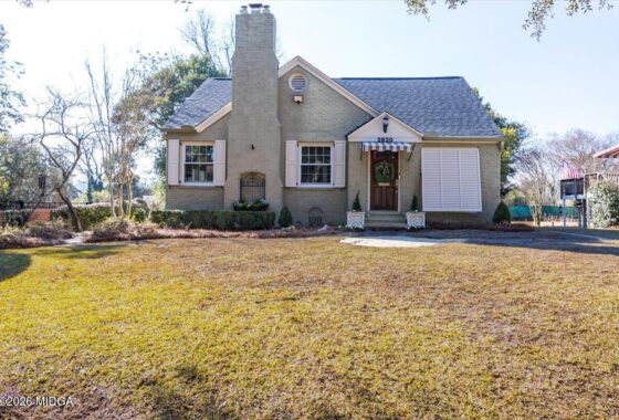 Front of a light-gray brick house with a chimney, white shutters, and a striped awning over the front door (address 2620)