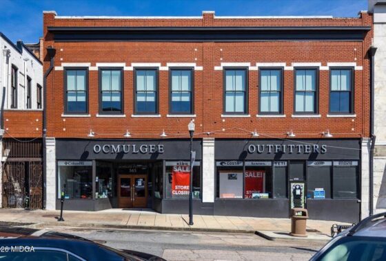 Brick storefront for OCMULGEE OUTFITTERS on a two-story brick building with large display windows and sale signs in the windows.