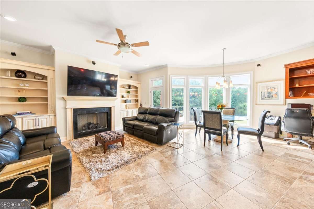 Open-concept living room with a gas fireplace, wall-mounted TV, and built-in shelves flanking the fireplace; black leather seating and a shag rug.