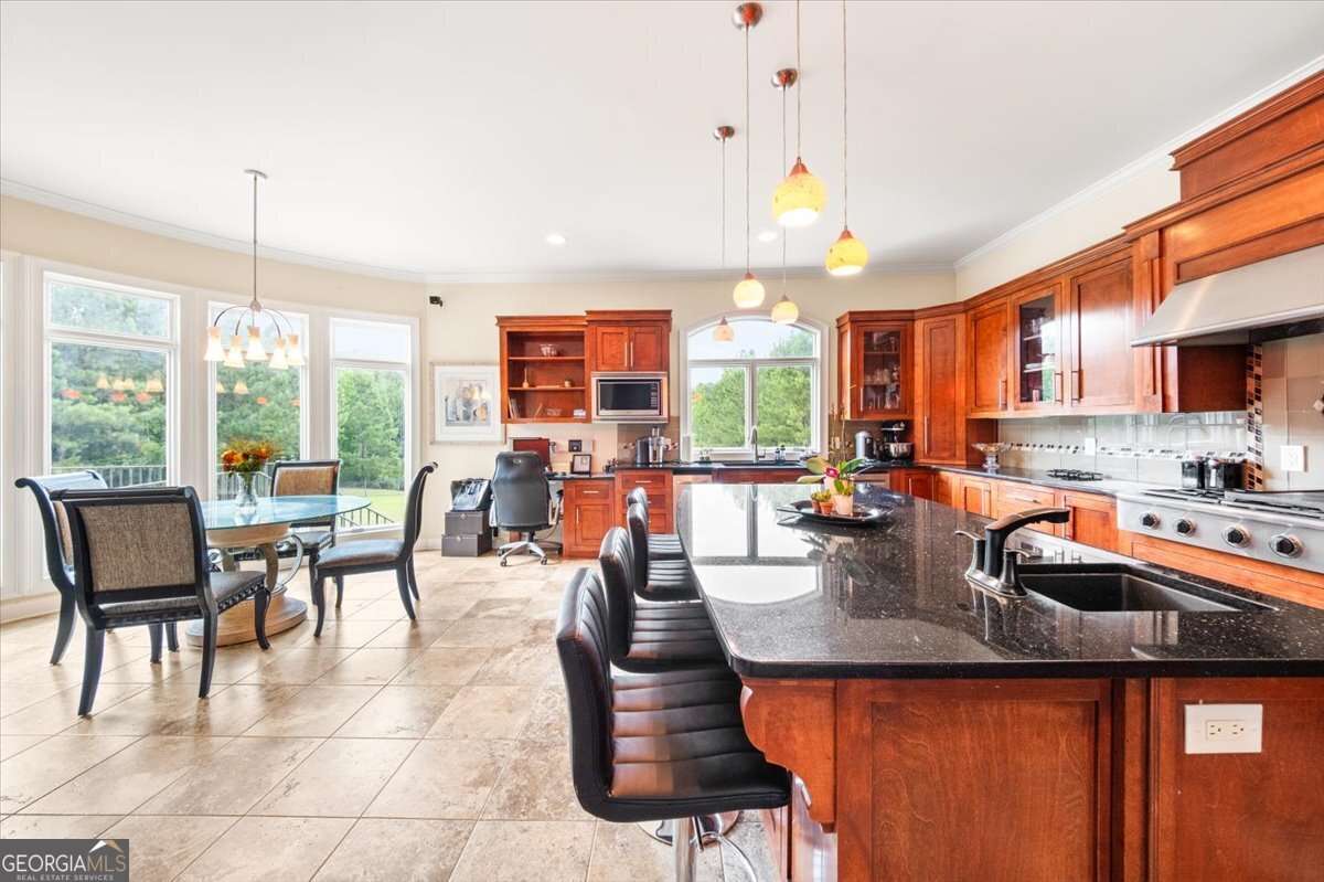 Open-concept kitchen with a dark granite island, cherry wood cabinets, and a dining area by large windows overlooking greenery.