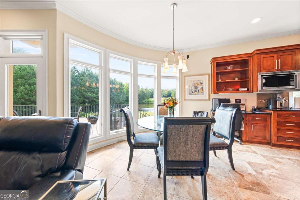 Bright dining area with a glass round table and four upholstered chairs beside curved bay windows overlooking a green outdoor view and outdoor balcony railing.