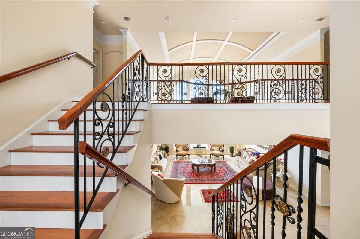 Two wooden staircases with decorative wrought-iron railings surround a bright open living room area.