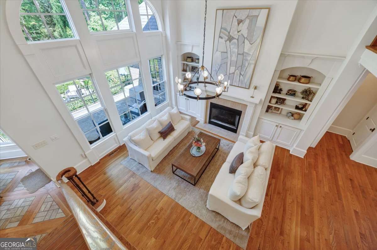 Bright two-story living room with white sofas, large arched windows, and a fireplace under a tall art piece.