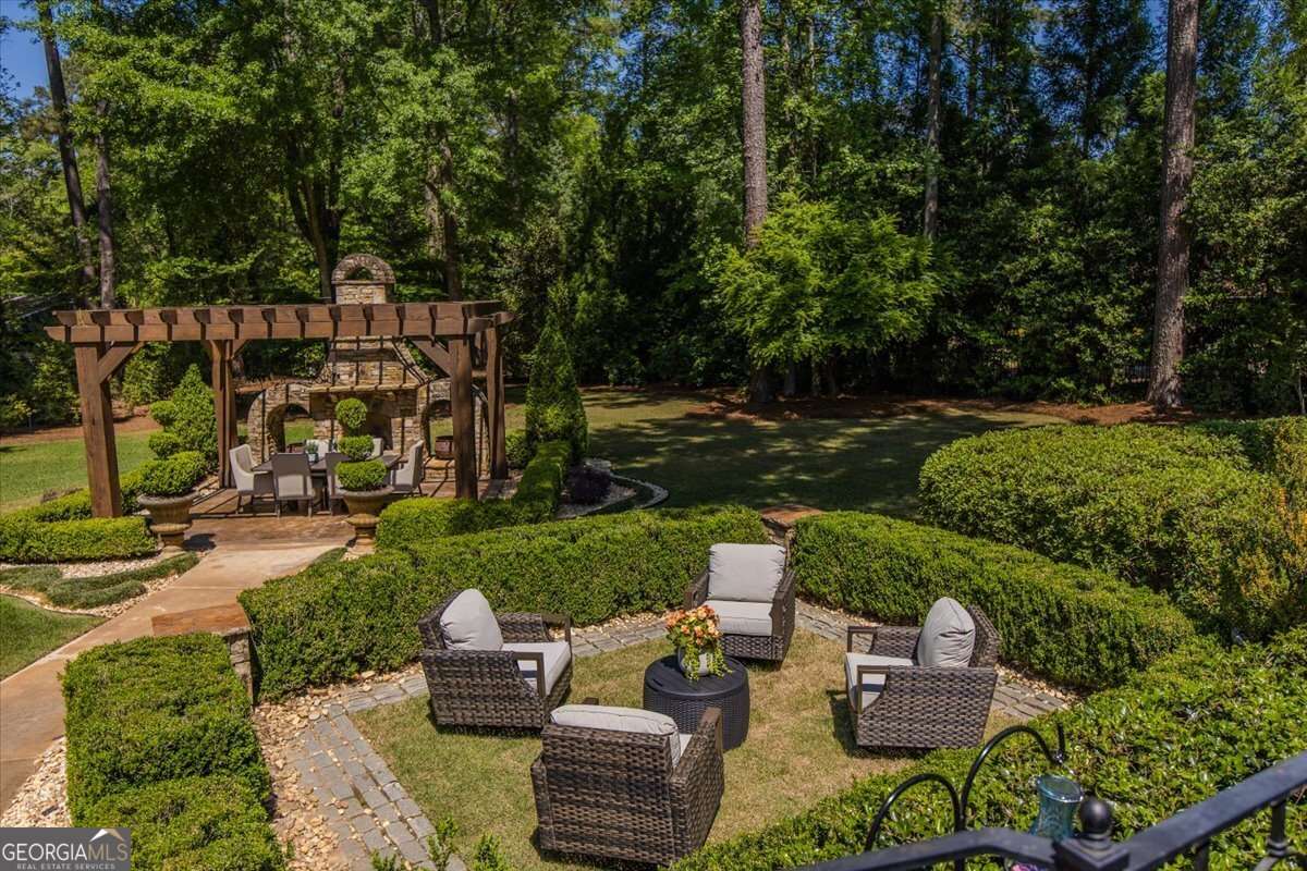 Backyard with a wooden pergola, stone outdoor fireplace, and dining area surrounded by trimmed hedges.