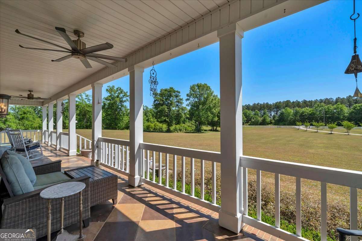 Front porch at 6605 Britt Road in Macon GA featuring comfortable seating, a ceiling fan, wooden railings, and views overlooking the landscaped lawn and surrounding trees.