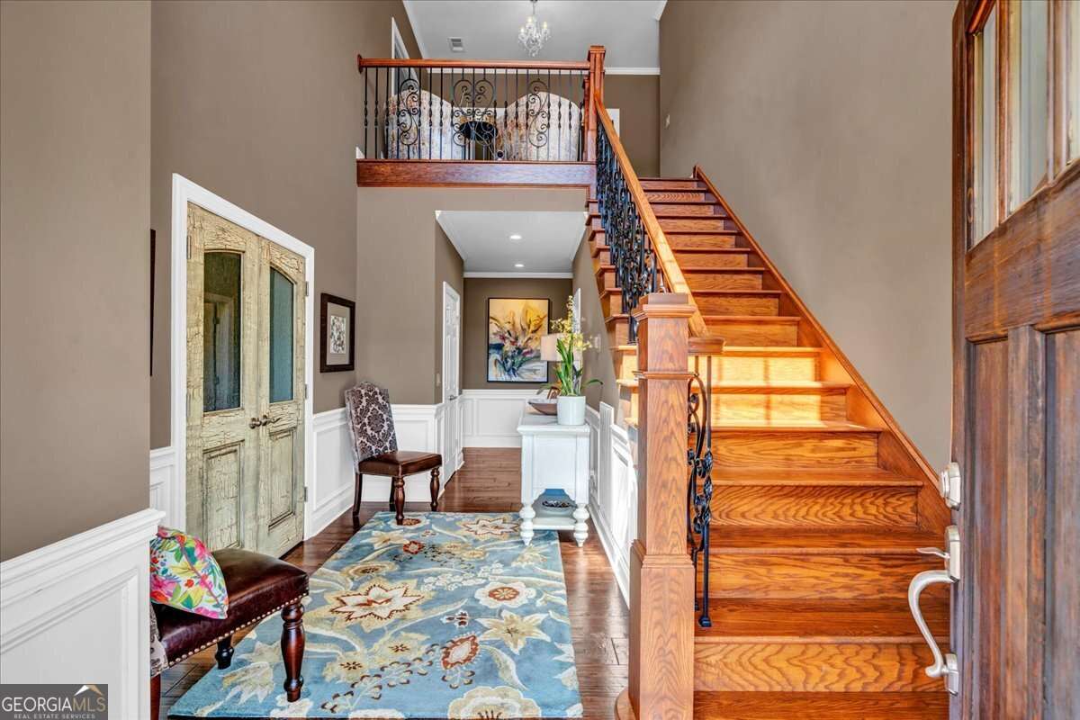 Front entry at 6605 Britt Road in Macon GA 31216 featuring a custom wood staircase with iron balusters, finely finished double entry doors, high ceilings, chair rail detailing, and rich hardwood flooring.