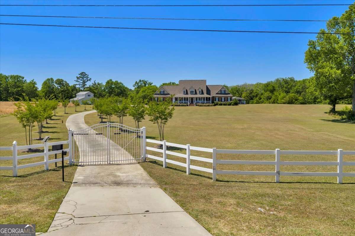 Gated entryway at 6605 Britt Road in Macon, GA featuring iron gates, wood fencing, an expansive front lawn, a tree-lined driveway, and the main residence, set on approximately 35.77 acres of private land in Bibb County.