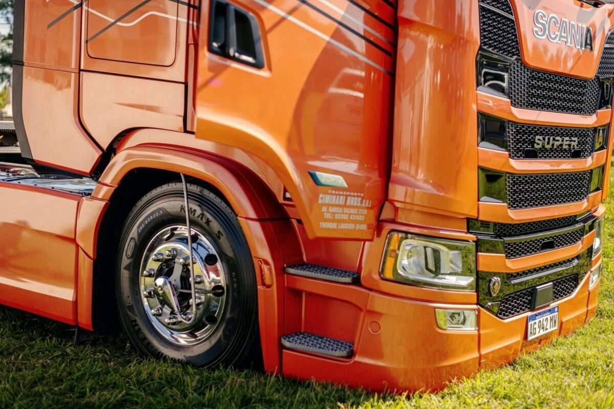 Orange Scania truck cab with a chrome wheel and grille, parked on grass edge.