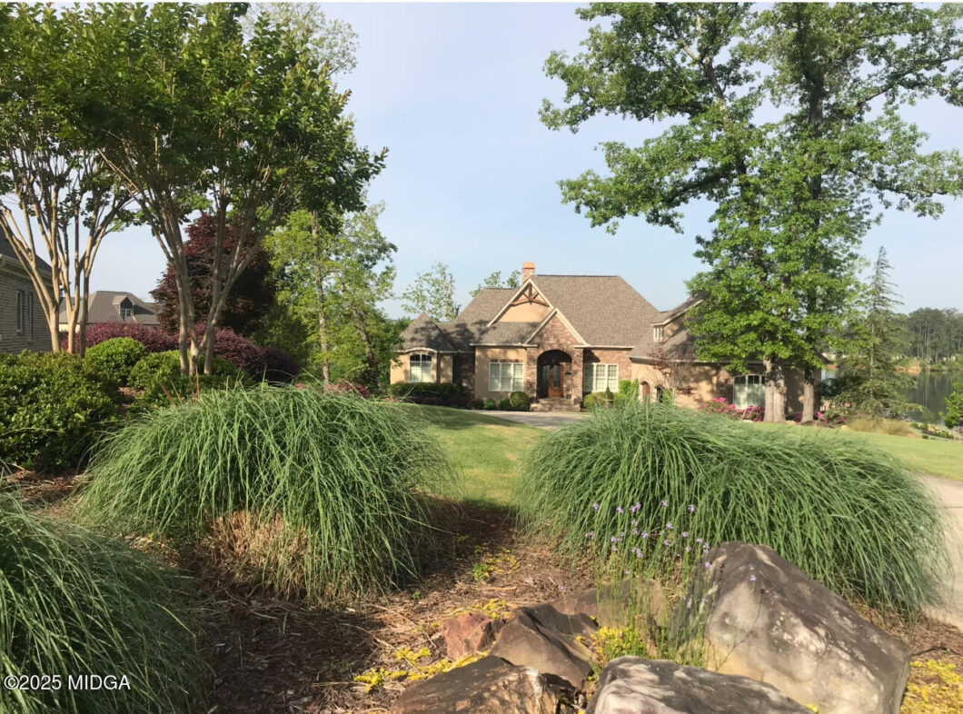 Brick house with aarched entryway framed by trees, front yard landscaping and a lake in the background.
