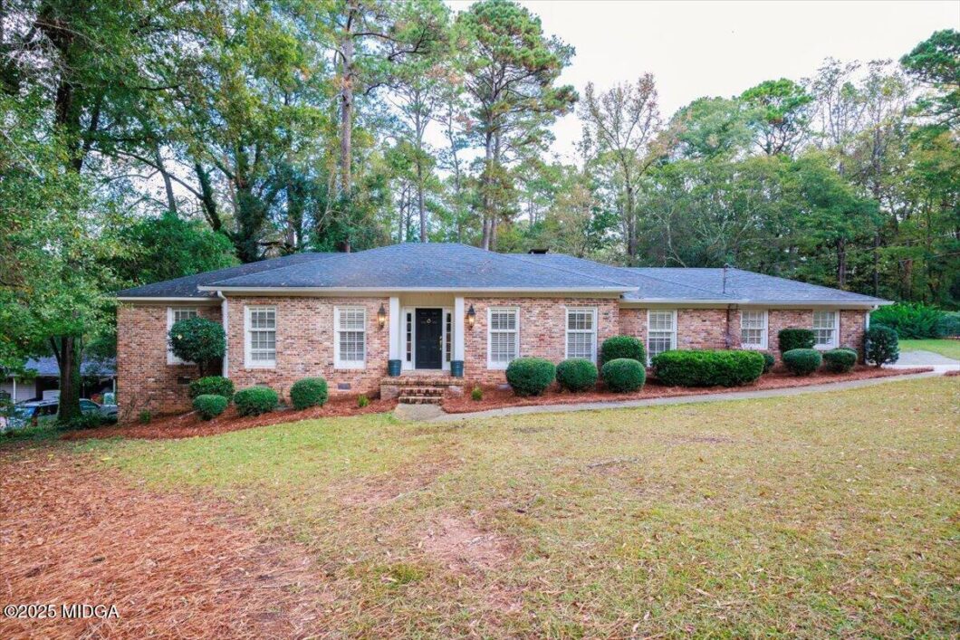 Single-story brick house with a black front door, white-framed windows, and manicured shrubs in front yard.