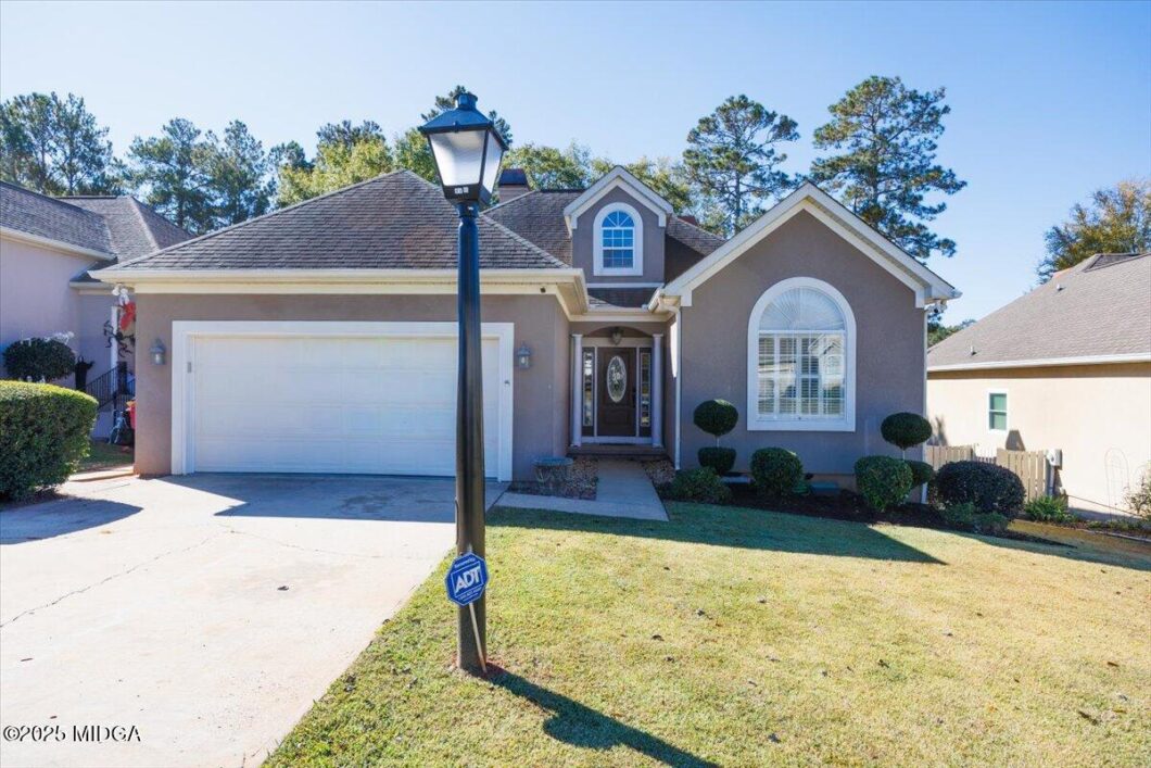 Front view of a suburban house with a two‑car garage and an ADT sign on a lamppost in the yard.