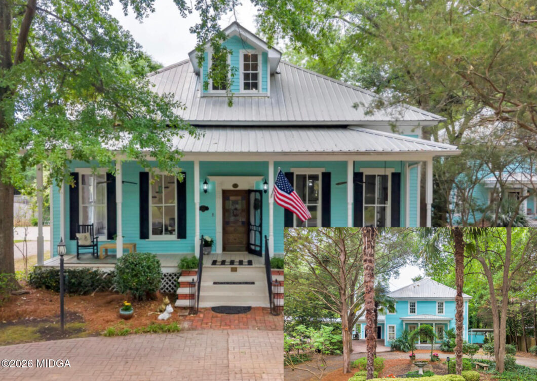 Turquoise two-story house with white trim and metal roof, front porch, and an American flag, surrounded by lush trees.