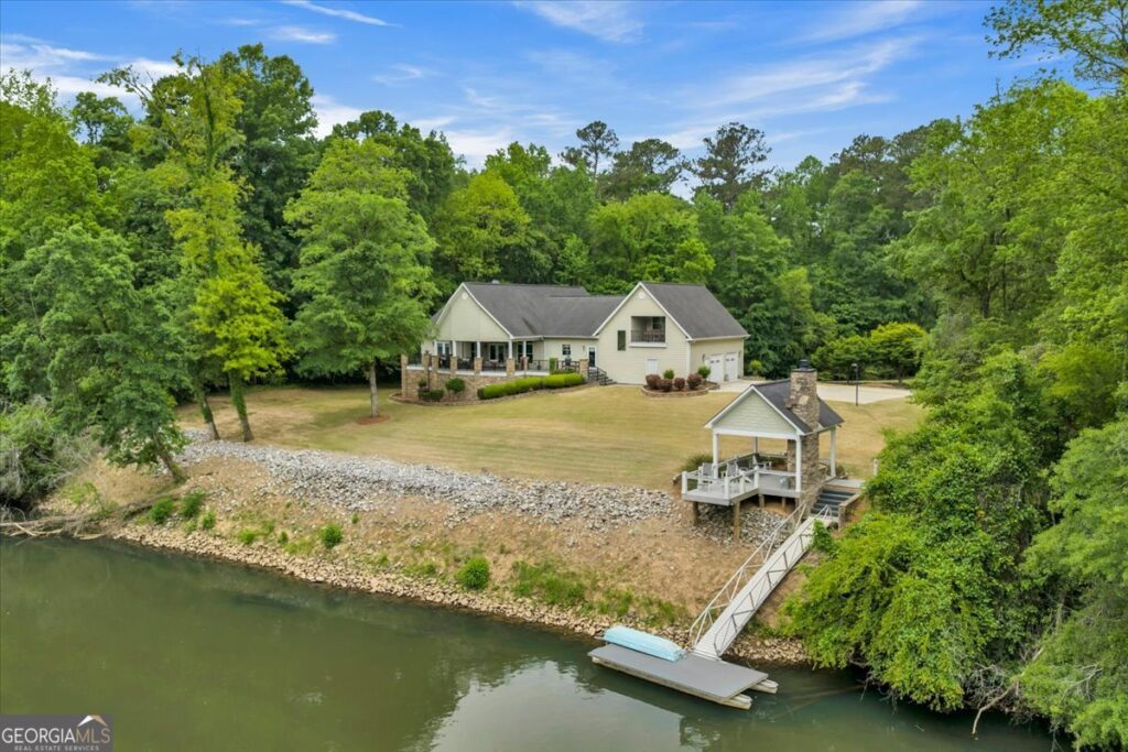 Aerial view of 625 Rum Creek Road in Juliette, GA featuring a private waterfront setting with dock, covered pavilion, expansive yard, and wooded surroundings.