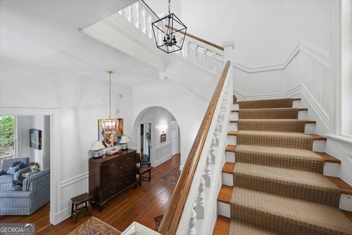 Bright, elegant foyer with a grand curved staircase, white wainscoting, hardwood floors, and modern lantern-style lighting, opening into adjacent living spaces.