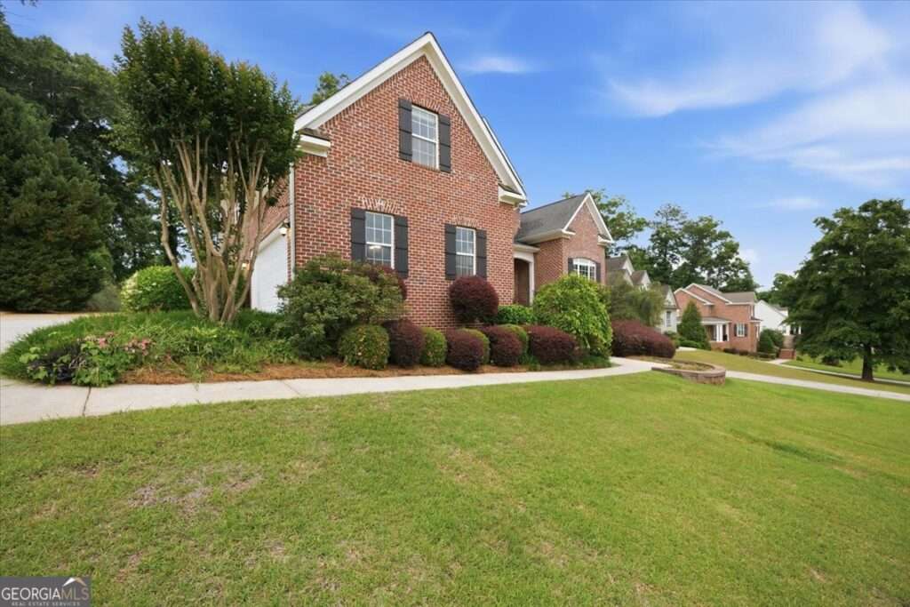 Brick two-story home with black shutters, a manicured front yard, and curved concrete walkway under a blue sky.