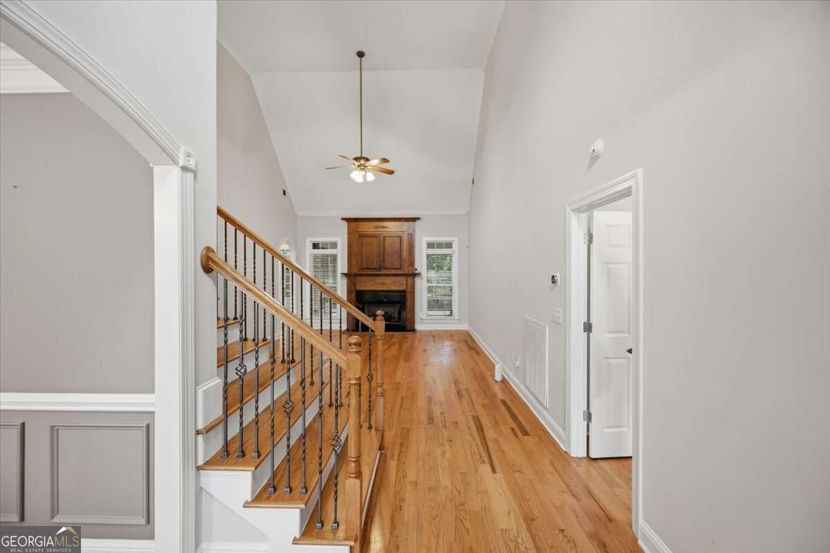 Bright two-story foyer with hardwood floors, a wooden staircase with iron balusters, and a stone fireplace at the far end.