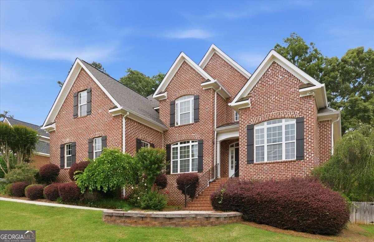 Front exterior of a stately three-level red brick home with gabled rooflines, black shutters, manicured landscaping, and a gently sloping lawn in Broadleaf Subdivision, North Macon.
