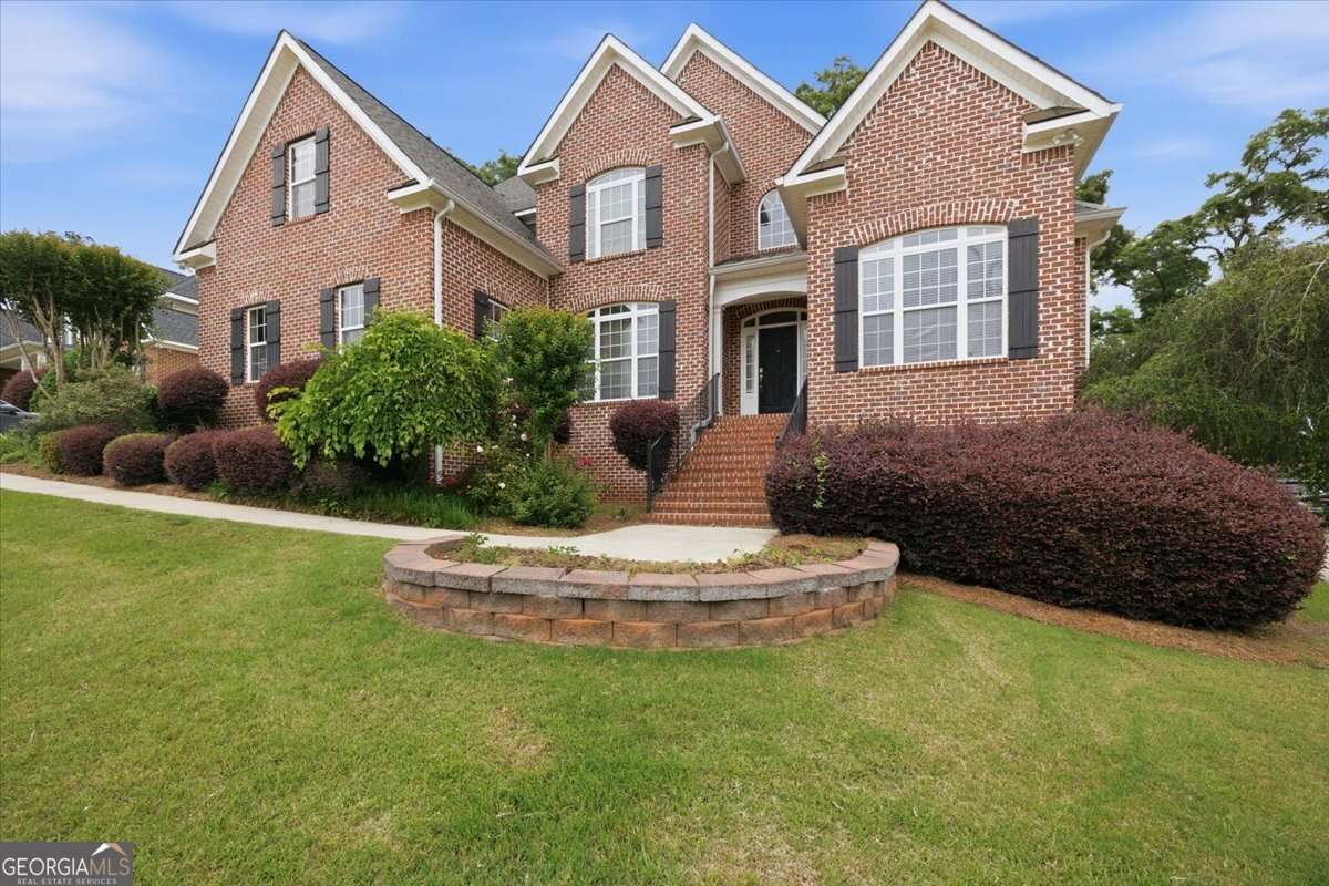 Brick two-story suburban house with arched entry, manicured shrubs, and a circular stone planter in the front yard.