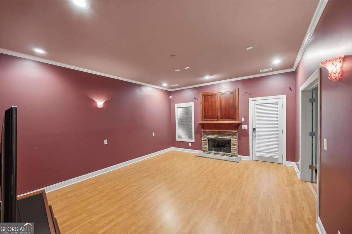 Spacious living room with purple walls, wood floor, and a stone fireplace below a wooden cabinet centerpiece.